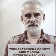 Melvin Roberts Older man with white hair, mustache and beard holding a jail booking card